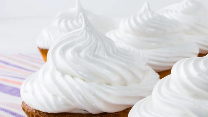 Cuatro cupcakes sin horno decorados con crema batida en forma de espiral sobre una mesa blanca y morada