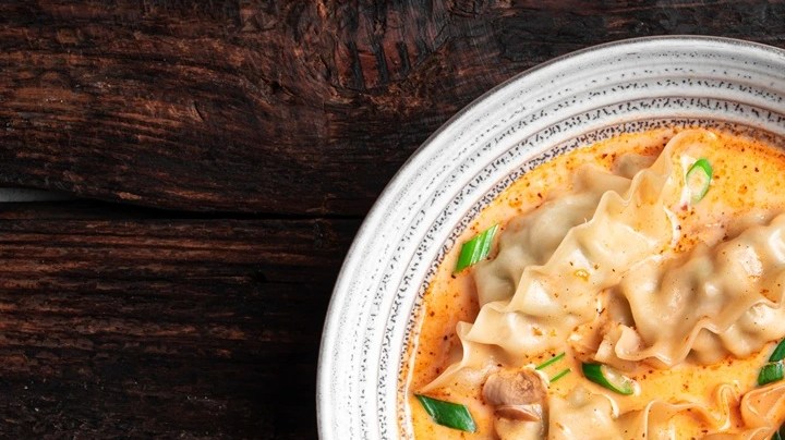 Plato blanco hondo con dumpling al horno en salsa de leche de coco y curry rojo