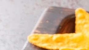 Plato hondo con ensalada cowboy sobre una bandeja de madera decorada con una cuchara y nachos