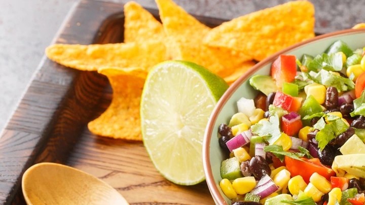 Plato hondo con ensalada cowboy sobre una bandeja de madera decorada con una cuchara y nachos