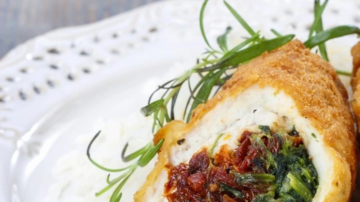 Plato decorado con perejil con unos rollos de pollo con jamón serrano, espinacas y queso