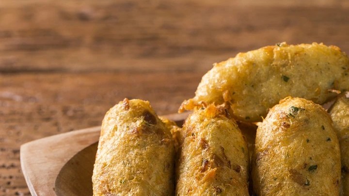 Varias unidades de buñuelos de cebolla y bacalao en un plato sobre una mesa de madera