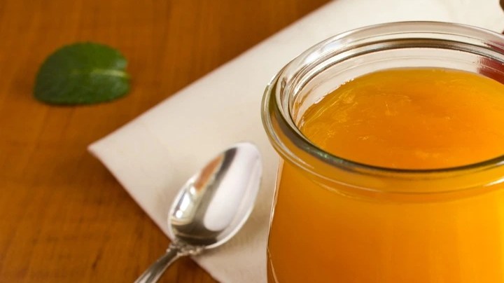 Frasco de vidrio con compota de mango, sobre una mesa de madera, decorada con cucharas y mangos