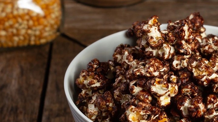 Recipiente blanco hondo sobre una mesa de madera con palomitas con chocolate
