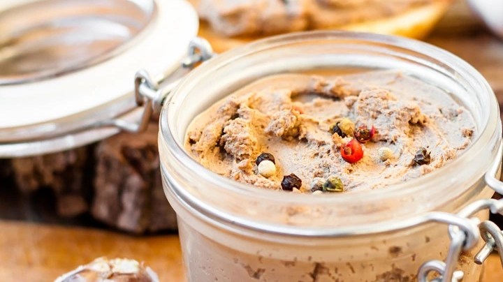 Recipiente de vidrio con paté de faisán sobre mesa de madera decorado con hierbas