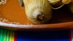 3 tamales colorados sobre un plato de cerámica en una mesa de color azul