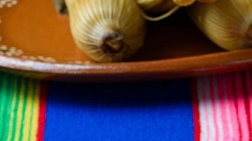 3 tamales colorados sobre un plato de cerámica en una mesa de color azul