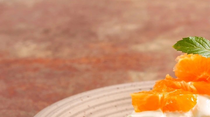 Pedazo de cheesecake de naranja decorado con gajos de naranja sobre un plato marrón