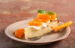 Pedazo de cheesecake de naranja decorado con gajos de naranja sobre un plato marrón