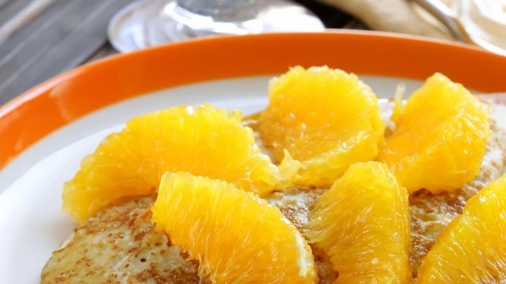 Pancakes de naranja y limón sobre un plato blanco con gajos de naranja decorados