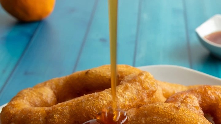 Picarones de camote con miel en un plato blanco sobre una mesa azul