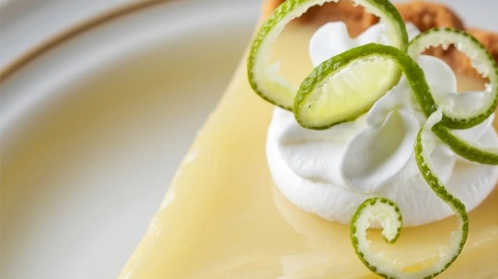 Cheesecake de lima sobre un plato blanco decorado con crema batida y lima