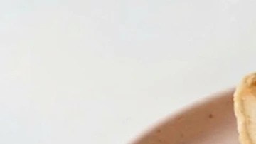 Halva cheesecake sobre un plato rosado, fresas picadas y una cuchara con un trozo de tarta