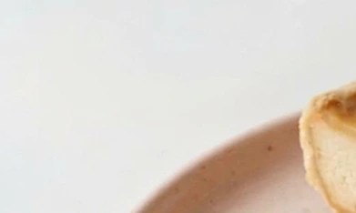 Halva cheesecake sobre un plato rosado, fresas picadas y una cuchara con un trozo de tarta