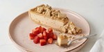 Halva cheesecake sobre un plato rosado, fresas picadas y una cuchara con un trozo de tarta
