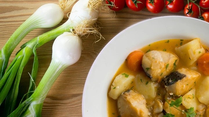 Merluza guisada con verduras en un plato blanco