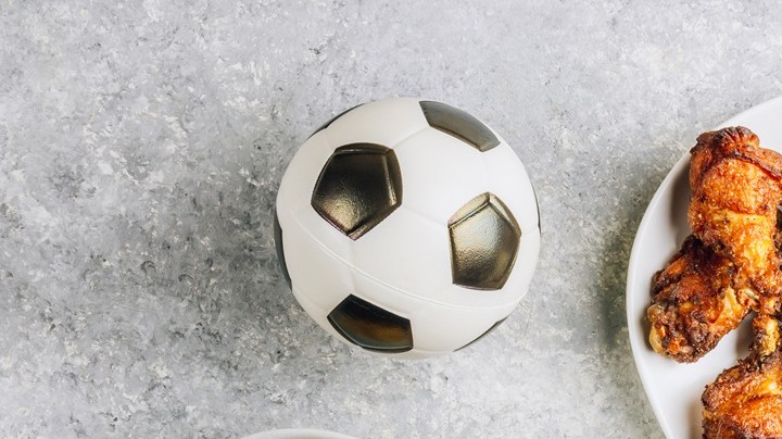 Un plato blanco con alitas de pollo, salsas y papas fritas con un balón de fútbol soccer