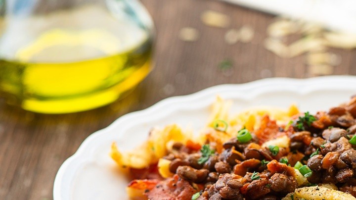 Plato blanco en una mesa de madera con guiso de fideos con lentejas