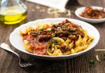 Plato blanco en una mesa de madera con guiso de fideos con lentejas