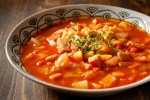 Guiso de fideos con papa y chorizo en un plato hondo sobre una mesa de madera